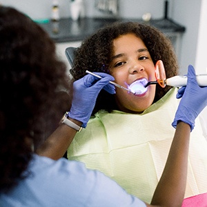 A dental hygienist uses a curing light to bond the tooth-colored filling into place on a young girl’s smile