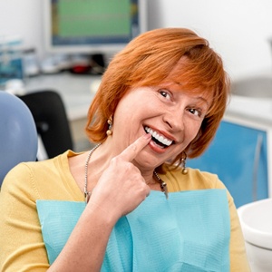 A woman pointing to her smile while in the dentist chair