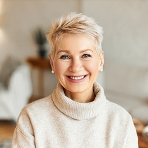 An older woman wearing a cream-colored sweater and smiling because of her new prosthetics