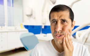 Man holding his cheek in pain before seeing an emergency dentist in East Islip